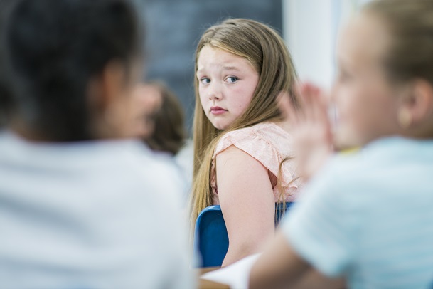 A young girl in class hearing two of her classmates whispering behind her