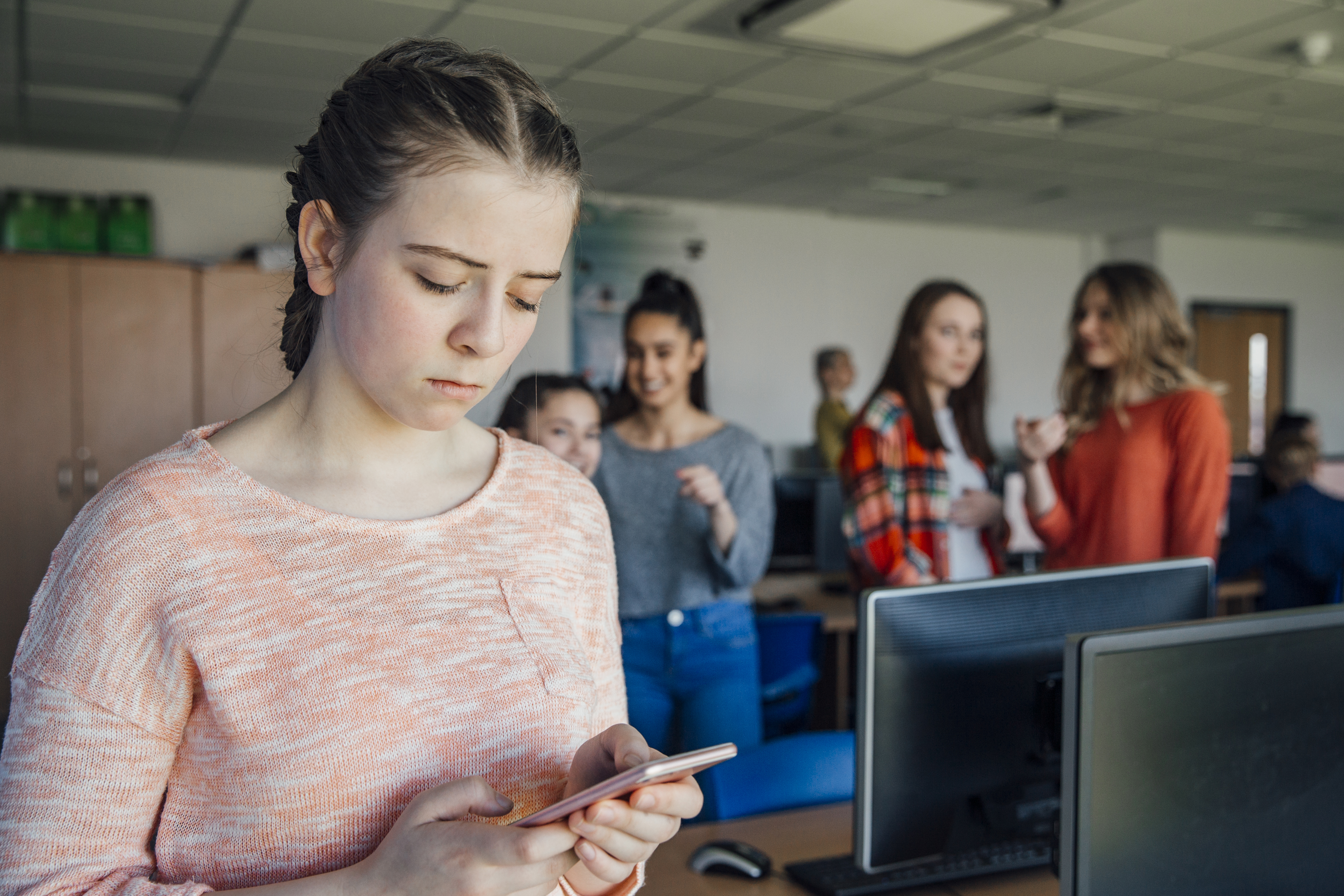 teenage girl in class looking at her phone, upset by the messages she sees