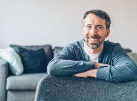 40ish man in his own place, on his couch smiling