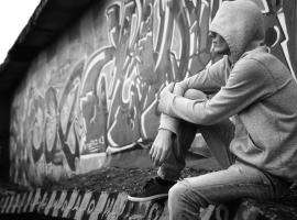 Hooded teen in front of graffiti wall